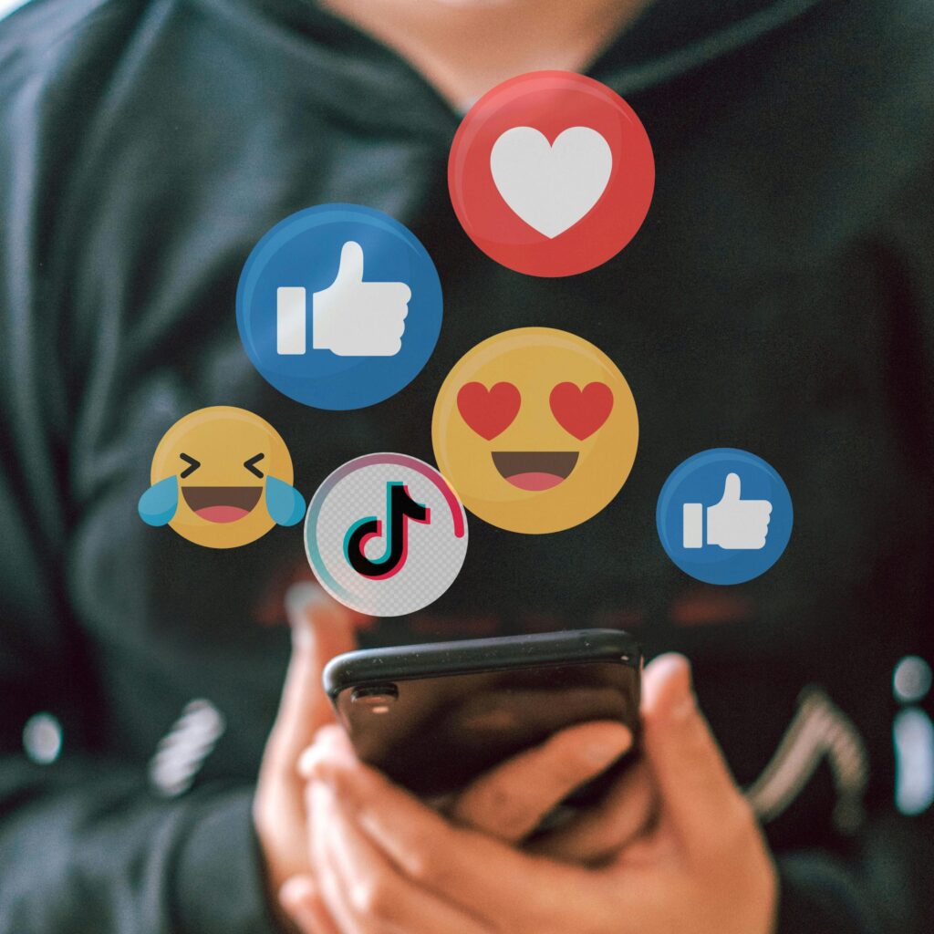 Person holding a smartphone surrounded by floating social media and reaction icons for social media video editing services
