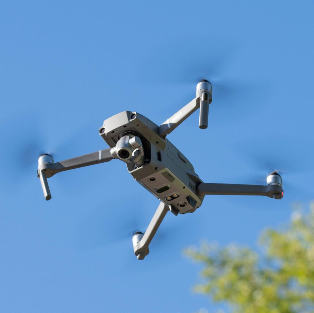 Drone hovering in flight against a clear blue sky for aerial photography and videography services.
